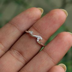 a person's hand holding a tiny ring with two diamonds on top of it