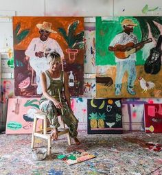 a woman sitting on a stool in front of paintings