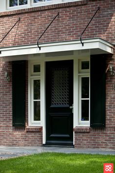 a black door and window in front of a brick building with green grass on the lawn