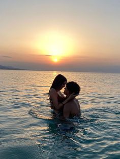 two people are sitting in the water at sunset, one is holding the other's head