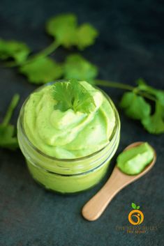 a jar filled with green food next to a wooden spoon