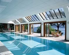 an indoor swimming pool surrounded by glass doors and windows with the ocean in the background