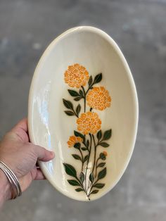 a hand holding a white bowl with orange flowers painted on the side and green leaves