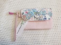 a pink and blue flowered wallet sitting on top of a white knit covered blanket