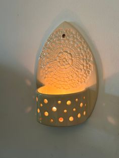 a white wall mounted candle holder with a lit candle in the center and small holes on it