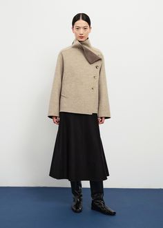 This jacket is perfectly boxy and minimal in silhouette thanks to a soft and structured layered wool melton construction. The jacket has a sleek asymmetric buttoned closure, dolman sleeves, and a mock neck collar with a folder flap detail showing a lovely tonal lining. Its unique construction pulls the right hand pocket to the front, and hides the left at the waist side. 100% wool. Model is 5ft 74 and wears size M. Chic Funnel Neck Outerwear For Work, Funnel Neck Wool Outerwear For Work, Modern Funnel Neck Outerwear For Fall, Wool Funnel Neck Outerwear For Work, Wool Outerwear With Funnel Neck For Work, Modern Structured Wool Coat, Asymmetrical Winter Office Outerwear, Modern Asymmetrical Outerwear For Work, Modern Asymmetrical Outerwear For Fall