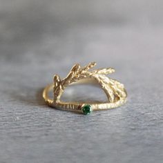 a gold ring with leaves and a green stone on the bottom, sitting on a table