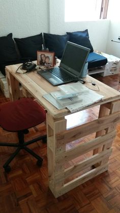 a laptop computer sitting on top of a wooden desk next to a red chair in a living room