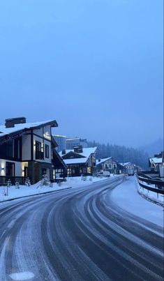 a street with snow on the ground and buildings in the background at night, lit up by lights