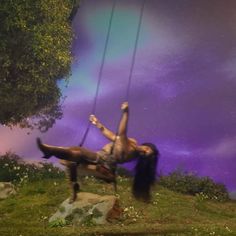 a woman is swinging on a swing in the air with her legs spread out and hands up