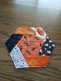 an orange and black hexagonal patchwork piece on a wooden table with pumpkins