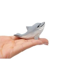 a hand holding a tiny toy dolphin in it's palm on a white background