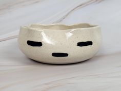 a white ceramic bowl with black dots on the side and eyes painted on the inside