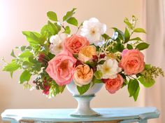 a vase filled with pink and white flowers on top of a blue table next to a window