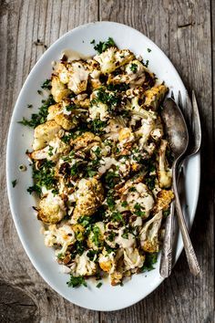 a white plate topped with cauliflower and parsley next to a silver fork