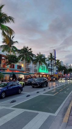 cars are driving down the street in front of buildings and palm trees at dusk time