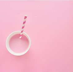 a pink and white paper cup with a striped straw sticking out of the top, on a pink background