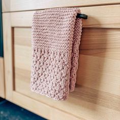 a pink knitted dish towel hanging on a wooden cabinet door with black handles and knobs