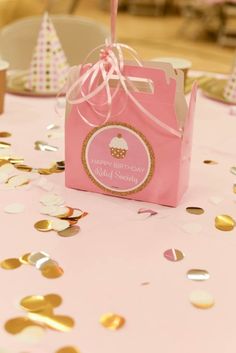 a pink bag with a cupcake on it sitting on a table surrounded by confetti