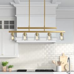 a kitchen with white cabinets and gold fixtures is pictured in this image, there are lights hanging from the ceiling over the stove