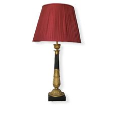 a lamp with a red shade on the side and a black base, sitting against a white wall