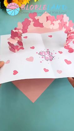 someone is holding up a paper cutout with pink hearts on it and the top half of