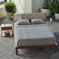 a bed sitting on top of a brick floor next to potted plants