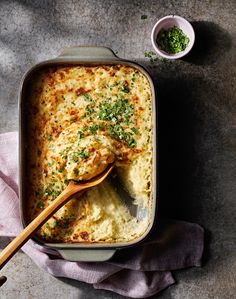 a casserole dish with cheese and parsley on the side next to a spoon