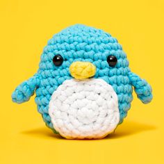 a crocheted blue bird sitting on top of a yellow background with black eyes