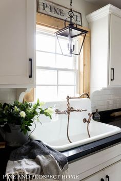 a white kitchen sink sitting under a window next to a vase with flowers on it