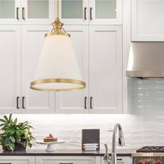 a kitchen with white cabinets and a gold pendant light over the stove top, surrounded by potted plants