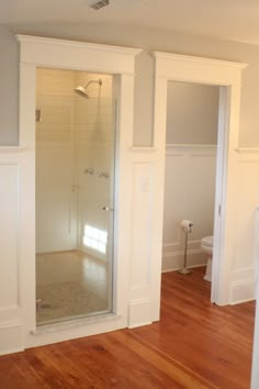 an empty bathroom with wood floors and white walls, including a walk in shower stall