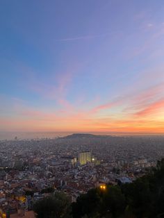 the sun is setting over a cityscape with buildings and hills in the background