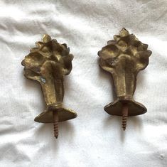 two brass scallop hooks are on a white sheet and one has a screwdriver in the shape of a flower