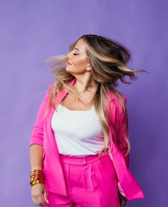 a woman with long hair wearing pink pants and a white top is posing in front of a purple background