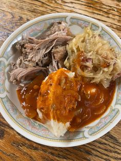 a white plate topped with meat and gravy next to coleslaw on a wooden table