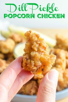 a hand holding up a piece of fried chicken in front of a bowl of lemon wedges