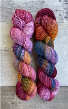 two skeins of yarn sitting next to each other on a wooden surface,