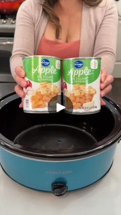 a woman holding two cans of food in front of an open crock pot on the stove