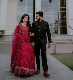 a man and woman standing in front of a large building wearing red dresses with sheer sleeves