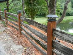 a wooden fence with two lights on it next to a river and trees in the background