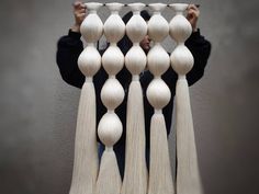 a person is holding up an art piece made out of wooden balls and tassels