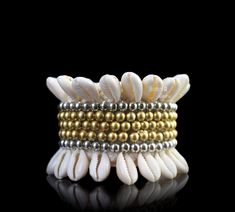 A Handmade Tribal Traditional New Guinea braided rope wide bracelet, decorated with two bands of cream Cowrie Shells, two bands of silver round beads, and three central bands of golden beads. The inner diameter of the bracelet is 2 inches (expands), and the maximum height of the bracelet is 2- 3/8 inches. The total length of the opened, flattened band of the bracelet is 6- 2/8 inches. The bracelet is finished, at each end, with two, approximately 5 inches cords (for adjustable sizing), each deco White Beaded Bohemian Cuff Bracelet, Handmade White Cuff Bracelet For Festival, Bohemian White Cuff Bracelet With Round Beads, Adjustable White Bohemian Cuff Bracelet, Bohemian Cream Bangle Jewelry, Bohemian Cream Adjustable Stretch Bracelet, Bohemian Cream Bangle, White Bohemian Stretch Bracelet For Festivals, Handmade Bohemian White Stretch Bracelet