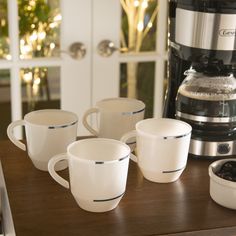 four coffee cups sitting on top of a counter next to an appliance and blender