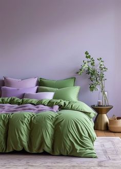 a bed covered in green and purple sheets with pillows on top of it next to a potted plant