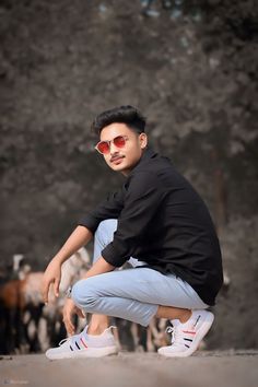 a man squatting down in front of a herd of cows wearing sunglasses and black shirt