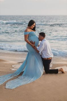 a pregnant woman standing next to a man on the beach with her belly wrapped up