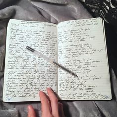 a person's hand holding a pen over a notebook with writing on the pages