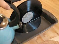 a person is holding a tea kettle and pressing the button on an old vinyl record