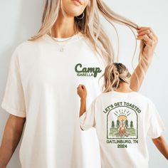 two women wearing camp t - shirts and one is holding her hair in the air